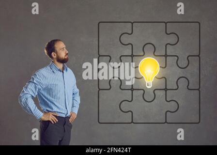 Mann betrachtet ein komplettes Puzzle mit einem hellen Idea Glühbirne in der Mitte Stockfoto