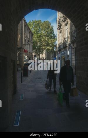 Zwei Menschen im Schatten kommen vom Markt in einer mittelalterlichen Straße im Stadtzentrum mit einem Baum im Hintergrund zurück Stockfoto