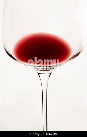 Vertikale konzeptuelle Nahaufnahme eines isolierten durchsichtigen Weinglas-Kelchblatts mit einem Rest Rotwein im Inneren auf weißem Hintergrund Stockfoto