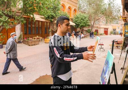 (210514) -- KASHGAR, 14. Mai 2021 (Xinhua) -- Mamattursunjian Mamatimen zeigt seine Bilder außerhalb seines Ateliers in der antiken Stadt Kashgar in der Autonomen Region Xinjiang Uygur im Nordwesten Chinas, 5. Mai 2021. Die dominante Farbe der Wohnungen in der antiken Stadt Kashgar in Xinjiang ist tiefgelb. Aber in den Werken des 26-jährigen lokalen Malers Mamattursunjian Mamatimen werden mehr Farben wie Orange, Weiß, Lila, Blau verwendet, um die Stadt zu malen. Das ist sein Lebensgefühl und auch ein Gefühl, das die Jugendlichen in Kashgar teilen, sagte Mamattursunjian. „Es braucht Mut, um durch das tr zu brechen Stockfoto