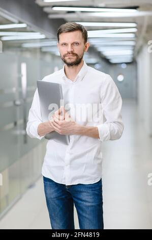 Porträt eines jungen Mannes in einem weißen Hemd im Büro. Der Manager im Büro hält einen Laptop in der Hand Stockfoto