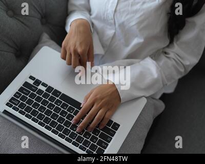 Aufnahme von weiblichen Händen, die auf der Laptop-Tastatur tippen Ihren Schoß, während sie auf dem Sofa saß Stockfoto