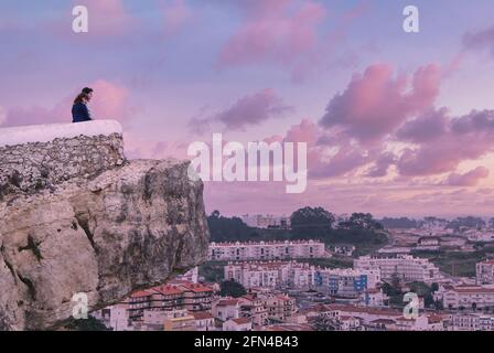 Atemberaubendes Foto eines romantischen Paares, das den Sonnenuntergang beobachtet. Zwei Liebhaber beobachten eine portugiesische Stadt von einem Aussichtspunkt aus. Liebe, Hoffnung und Purpur. Stockfoto