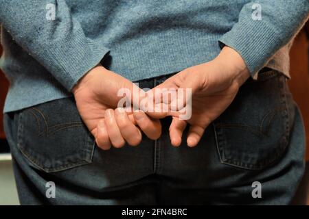 Eine ältere Frau hält ihre Hände hinter ihrem Rücken. Nahaufnahme einer Hand, die die beiden anderen Finger ergreift. Durchdachte Gesten. Stockfoto