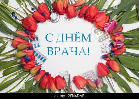 Ein Rahmen aus Tulpen und Medizintabletten mit Inschrift Übersetzung Vom russischen Happy Doctor's Day Stockfoto