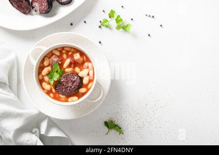 Traditionelle spanische Fabada mit Haricot, Speck oder gestreifem Speck, asturischer schwarzer Pudding auf weißem Hintergrund. Blick von oben. Speicherplatz kopieren. Asturiana Cu Stockfoto