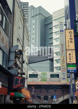 Die Tokyo Metro verläuft durch die Stadt und führt zwischen den Wolkenkratzern hindurch. Agglomerate von Gebäuden in der japanischen Hauptstadt. Chaotisches Leben und Restaurant Schild Stockfoto