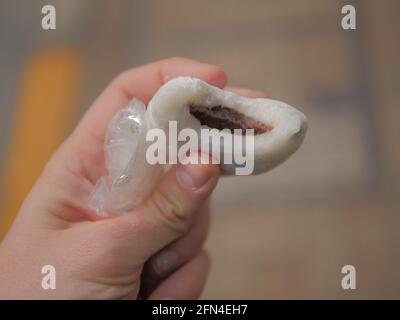 Die Hand hält einen Mame Daifuku Mochi, der auf der Straße gegessen wird. Traditionelles japanisches Reisdessert mit Sesambohnen. Süßes Gebäck mit Füllung. Stockfoto