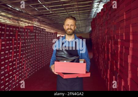 Glücklicher Schuhfabrikbesitzer oder Lagerverwalter, der einen Karton hält Mit schwarzen Lederstiefeln Stockfoto