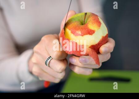 Nahaufnahme der Hände, die einen Apfel schälen. Die Hände der Frau entfernen die Haut eines roten Apfels mit einem Messer. Stockfoto