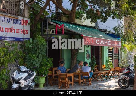 Vietnamesische Männer saßen vor dem malerischen Café in Da Nang, Vietnam, in Sonnenlicht getaucht Stockfoto