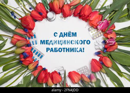 Ein Rahmen aus Tulpen und Medizintabletten mit einer Inschrift auf Russisch. Übersetzung: Happy Medical Worker Day. Stockfoto