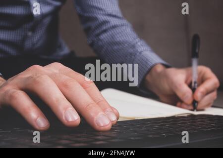 Persönliches Finanzierungskonzept. Der junge Mann plant in seinem Tagebuch. Listen oder Checkbögen erstellen. Nahaufnahme von Schreibhand und Tastatur. Getöntes Bild. Stockfoto