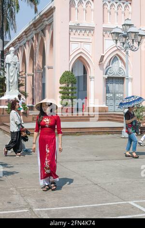 Attraktive weibliche Touristen tragen konischen Hut und traditionelle vietnamesische Ao dai Kleid in Da Nang Kathedrale (rosa Kirche), Da Nang, Vietnam Stockfoto