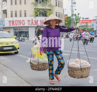 Vietnamesischer Straßenhändler mit konischem Hut trägt Snacks in zwei Körben mit Schulterstock, Da Nang, Vietnam Stockfoto