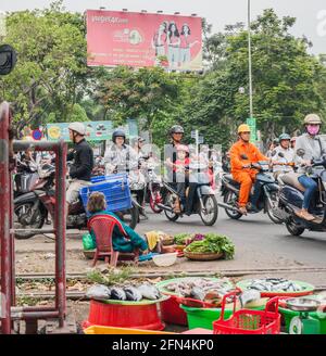 Straßenverkäufer, der frischen Fisch und Gemüse verkauft, während der Verkehr über die Bahnlinie in Da Nang, Vietnam, fährt Stockfoto