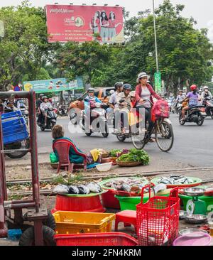 Straßenverkäufer, der frischen Fisch und Gemüse verkauft, während der Verkehr über die Bahnlinie in Da Nang, Vietnam, fährt Stockfoto