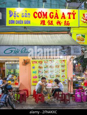 Vietnamesisches Paar sitzt auf dem Bürgersteig vor dem Restaurant mit graridem Essen Foto-Menü, Da Nang, Vietnam Stockfoto