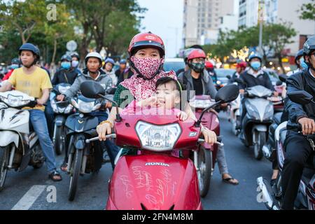 Mutter und Kind sitzen geduldig auf dem Roller und warten an der Straßenkreuzung darauf, dass sich die Lichter ändern, Da Nang, Vietnam Stockfoto