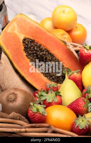 Korb mit tropischen Früchten, Orangen, Birnen Kiwi Papaya mit einem Mixer auf einem Holztisch. Vertikal Stockfoto