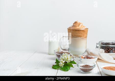 Dalgona Kaffee, Zutaten und Blumen auf weißem Hintergrund mit Platz zum Kopieren. Seitenansicht, horizontal. Stockfoto