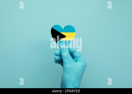 Hände mit schützenden chirurgischen Handschuhen, die das Herz der Bahamas-Flagge halten Stockfoto