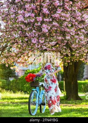 Sakura-Saison. Romantische Fahrradtour. Tourismuskonzept. Transport und Reisen. Mädchen langes Kleid Retro Cruiser Fahrrad Sakura Baum. Frühlingsferien Stockfoto
