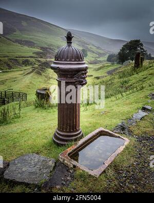 Alter rostiger gusseiserner Trinkbrunnen mit dekorativem Löwenkopf Muster und ein Keramikbecken, das bei Wanlockhead in den Boden gesunken ist In den Leadhills Stockfoto