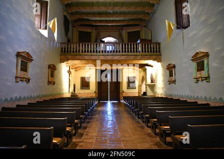 Das Innere der Kapelle der Missionsbasilika San Diego de Alcalá mit den dunklen Eichenbänken, dem Terrakotta-Fliesenboden und dem restaurierten Altar in Kalifornien, USA. Stockfoto