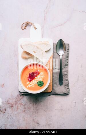 Schüssel mit Tomatensuppe aus Salmorejo mit Schinken und gekochtem Ei auf einem Marmor- und Holzbrett mit Brotscheiben und einem Löffel auf einer Serviette. Gazpacho traditionell Stockfoto