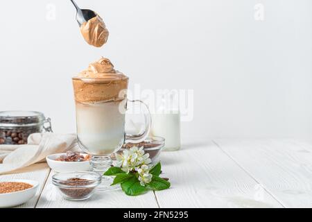 Dalgona Eiskaffee und Schaumlöffel auf weißem Hintergrund mit Zutaten und Farben. Seitenansicht, horizontal. Stockfoto