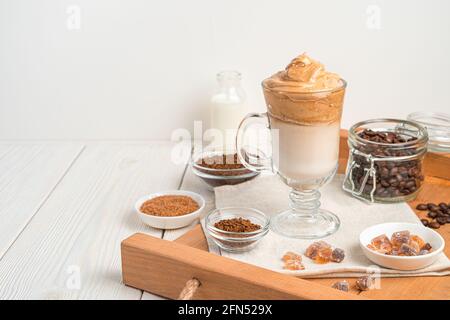 Kalter Dalgona-Kaffee auf einem braunen Tablett mit Zutaten. Seitenansicht, Kopierbereich. Stockfoto