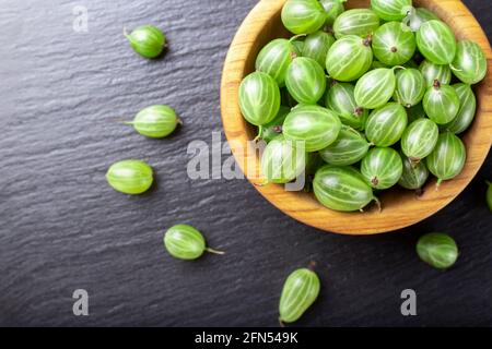 Frische Stachelbeeren in Holzschale auf schwarzem Stein Schiefer Hintergrund. Draufsicht. Stockfoto