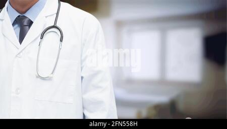 Zusammensetzung des mittleren Abschnitts des männlichen Arztes im Laborkittel mit Stethoskop über Krankenhaus außer Fokus Stockfoto