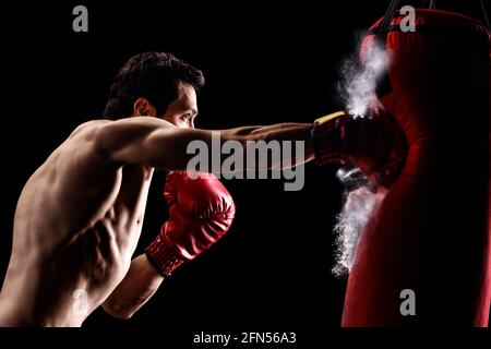 Starker, muskulöser Mann Stanzen einen Beutel mit Boxhandschuhen auf schwarzem Hintergrund Stockfoto
