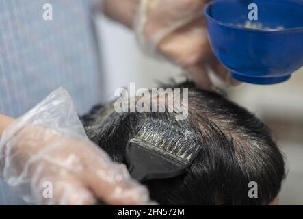 Friseur mit Einweg-Plastikhandschuhen, die die Haarwurzeln einer Frau färben Mit einer Haarbürste Stockfoto