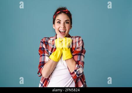 Lächelnd aufgeregt attraktive junge Frau in Schürze und Gummihandschuhe Isoliert auf blauem Hintergrund stehend Stockfoto