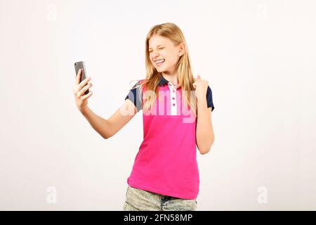 Glückliche, schöne junge, glückliche Frau mit natürlichen, langen blonden Haaren, die ihren Sieg feierten, schreiend und lachend auf ihren Smartphone-Bildschirm schauten. Teenager Stockfoto