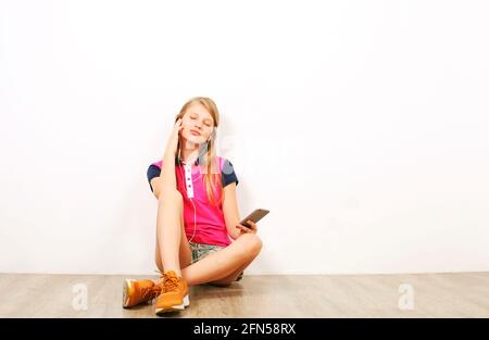 Schönes Teenager-Mädchen auf Holzboden sitzen und Lieblingslied auf Handy-Musik-App von ihrem Handy hören. Casual junge weiblich genießen geliebten t Stockfoto