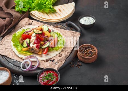 Fleisch, gebratene Kartoffeln, Gemüse, Salat und Sauce auf einer dünnen Pitta auf einem braunen Schneidebrett. Vorbereitung von Tacos, Shawarma, Burritos. Seitenansicht, kopieren Stockfoto