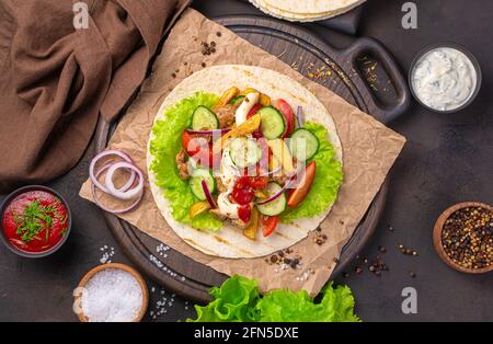 Mexikanische Tacos auf braunem Hintergrund. Tortilla, Fleisch, Pommes Frites, Gemüse und heiße Sauce. Stockfoto