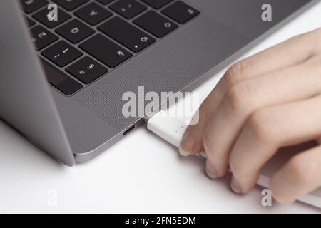 Nahaufnahme eines Typ-C-Kabels, das mit einer weiblichen Hand mit dem Laptop verbunden ist. Minimalistisch Stockfoto