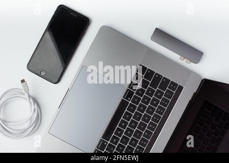 Draufsicht Foto eines schwarzen Smartphones, usb-Typ-C-Kabels, usb-Hub und eines Laptops auf weißem Hintergrund. Stockfoto