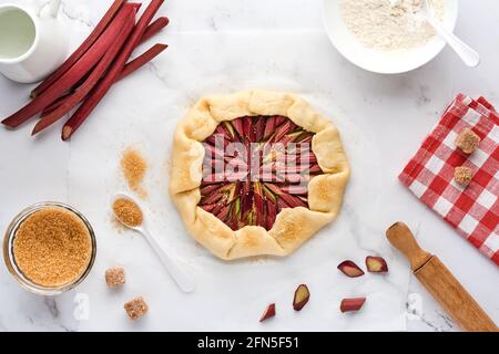 Galette mit frischem Rhabarber Prozess der Zubereitung und Zutaten Mehl, Wasser, Butter, Zucker und Rhabarber zum Backen auf weißem Marmor Hintergrund. Chris Stockfoto