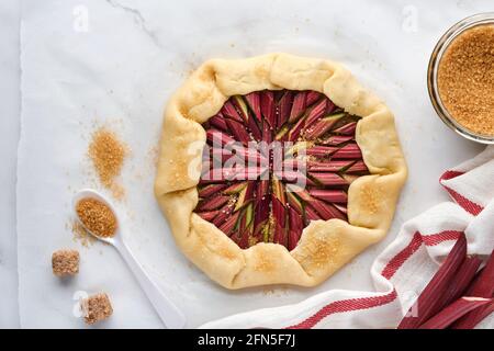 Galette mit frischem Rhabarber Prozess der Zubereitung und Zutaten Mehl, Wasser, Butter, Zucker und Rhabarber zum Backen auf weißem Marmor Hintergrund. Chris Stockfoto