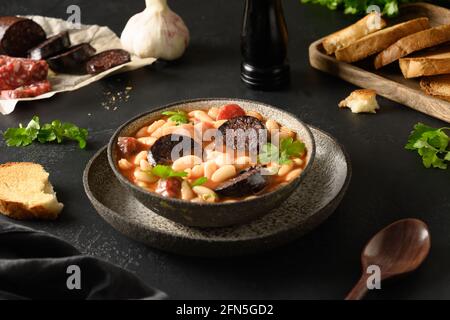 Beliebte spanische Fabada mit Chorizo, Morcilla, Wurst, Haricot serviert frischen Toast auf schwarzem Hintergrund. Asturischer Bohneneintopf. Nahaufnahme. Stockfoto