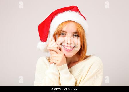 Nahaufnahme Porträt der schönen rothaarigen jungen Frau trägt Weihnachtsmann Hut & weißen Pullover mit zufriedenen Gesichtsausdruck. Niedliche weibliche feiern Stockfoto