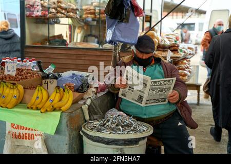 Übergewichtiger georgischer Mann. Ein Straßenmarktverkäufer liest eine Zeitung, während er an der Theke sitzt. Tiflis, Georgien - 03.16.2021 Stockfoto