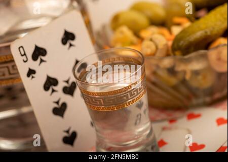 Spielkarten, ein Glas Wodka, ein Dekanter Wodka und eine Glasschale mit Gurken und Pilzen auf dem Tisch. Nahaufnahme, selektiver Fokus. Stockfoto