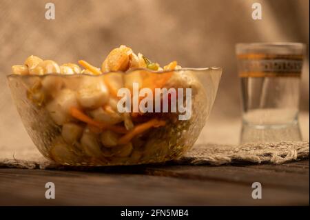 Eingelegte Pilze in einer Glasplatte und ein Becher Bier auf einem Tisch, der mit einem Tuch mit rauer Textur bedeckt ist. Nahaufnahme, selektiver Fokus. Stockfoto